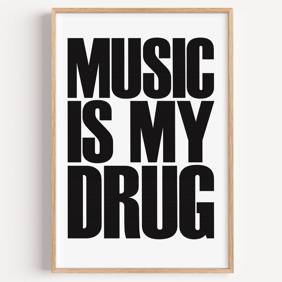 Music Is My Drug black lettering on white print in a light oak frame on a plain white wall