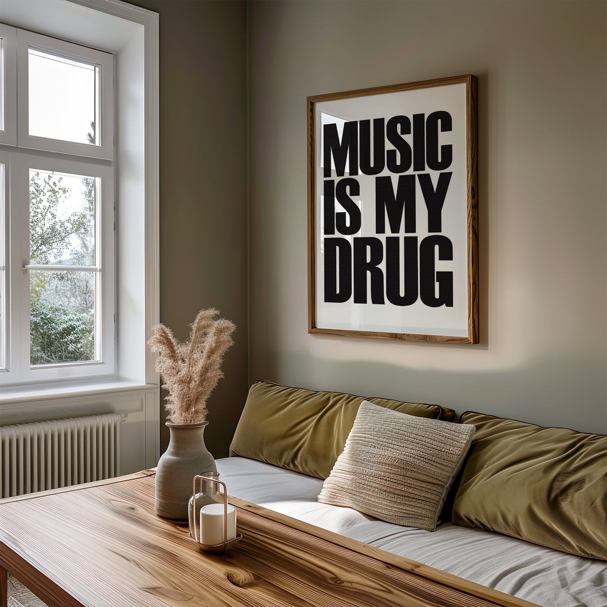 Music Is My Drug black lettering on white print in a walnut frame above an olive daybed by a window