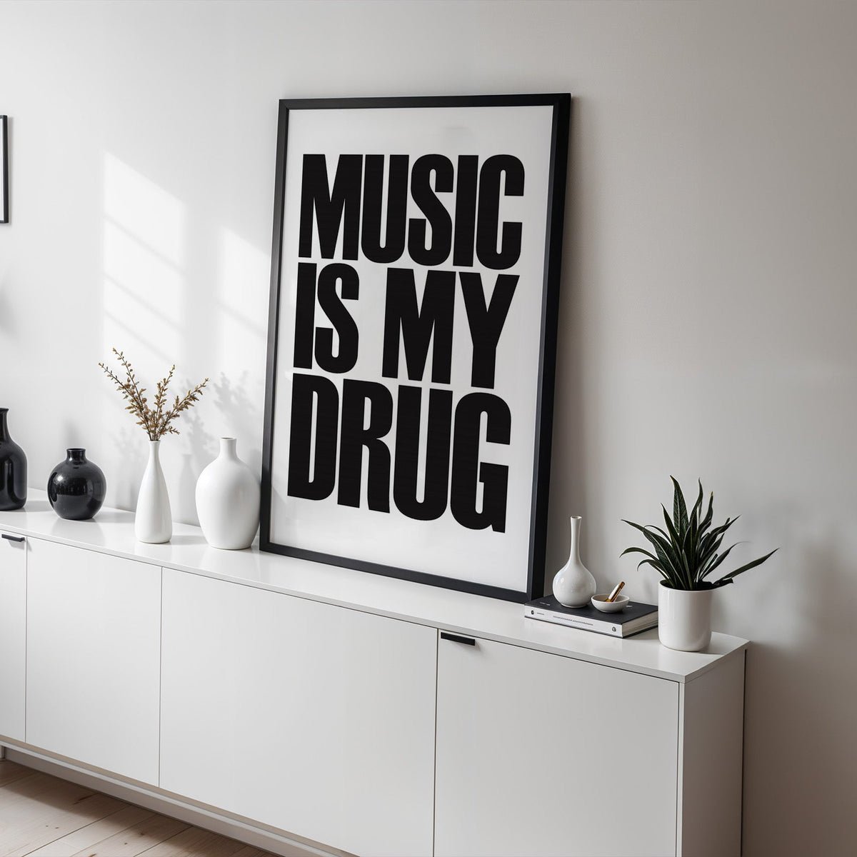 Music Is My Drug black lettering on white print in a black frame on a white sideboard with black and white vases