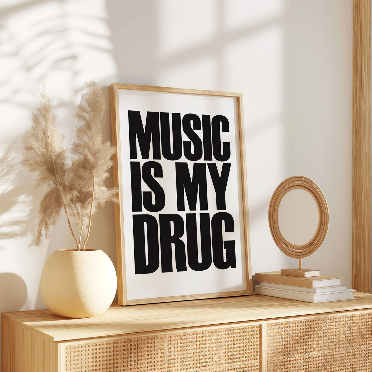 Music Is My Drug black lettering on white print in an oak frame on a rattan sideboard beside pampas grass