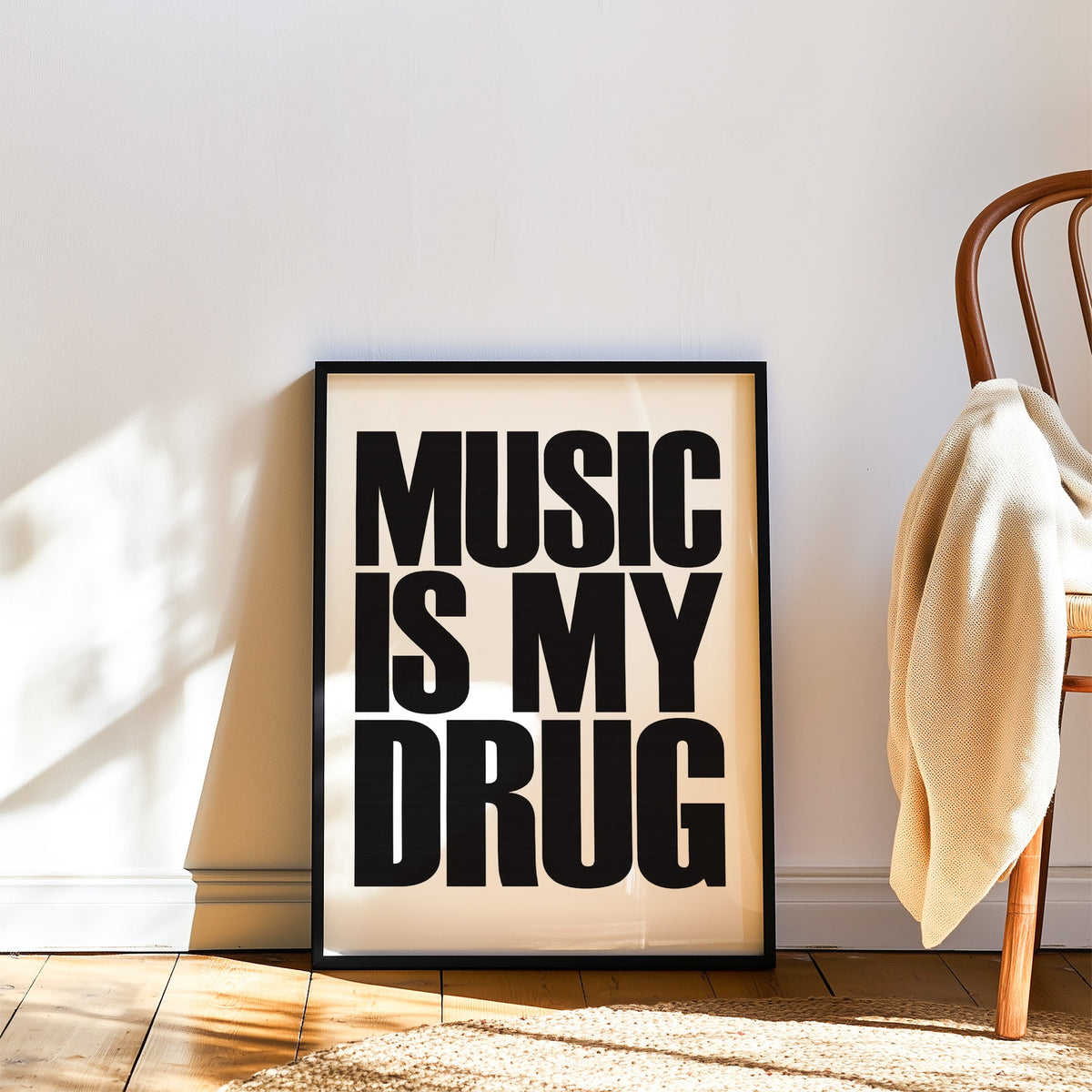 Music Is My Drug black lettering on white print in a black frame leaning on a wood floor beside a bentwood chair