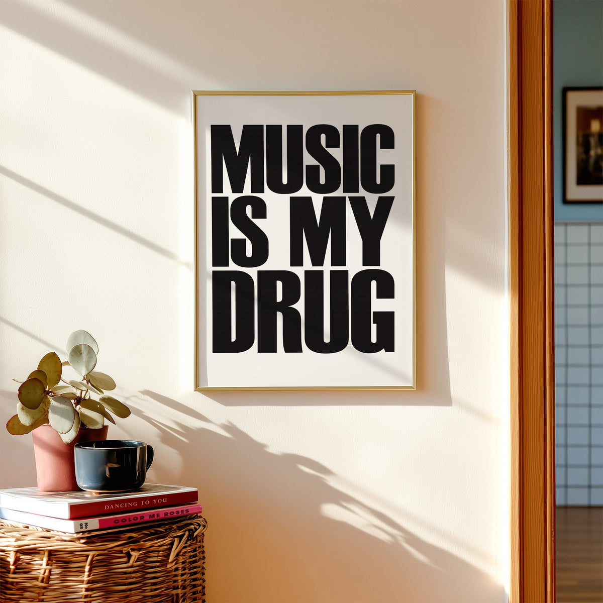 Music Is My Drug black lettering on white print shown in a gold frame above a wicker basket and stacked books