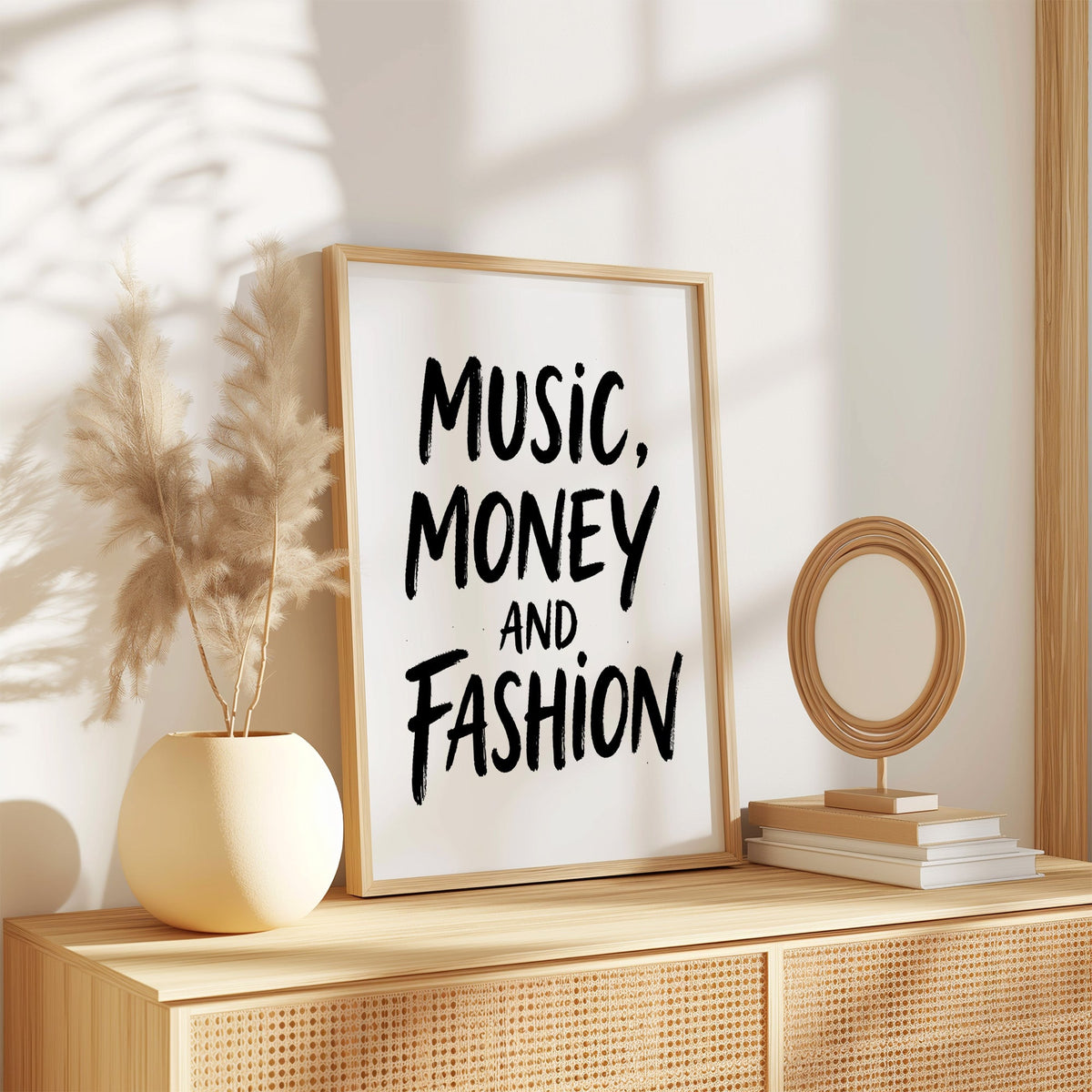 Music, money and fashion brush lettering print in an oak frame on a rattan sideboard beside pampas grass