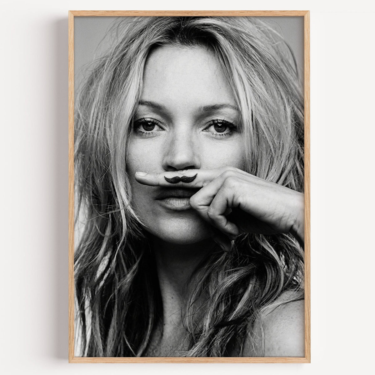 Close portrait with finger mustache under nose print in a light oak frame on a plain white wall