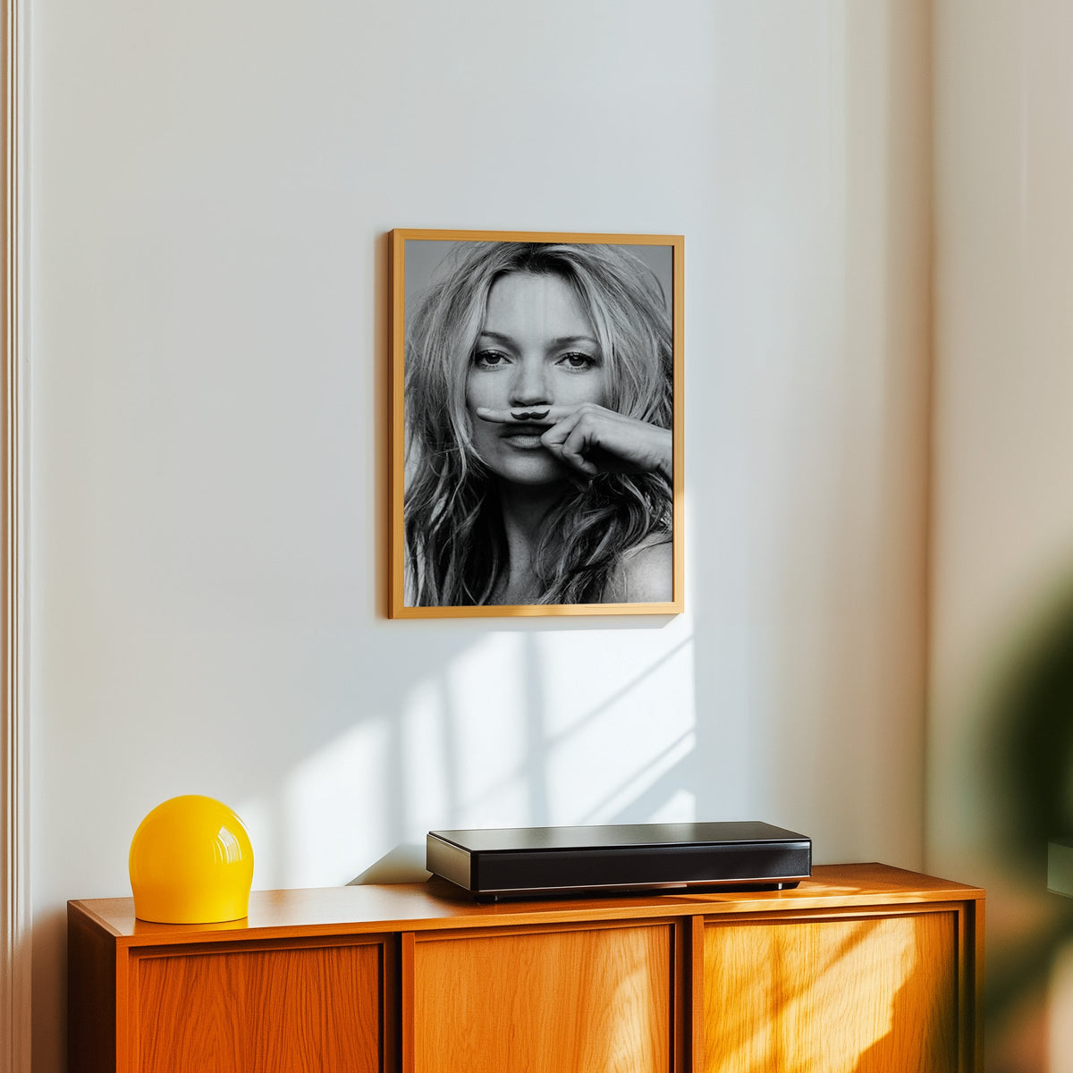 Close portrait with finger mustache under nose print in an oak frame above a teak sideboard with a yellow glass lamp