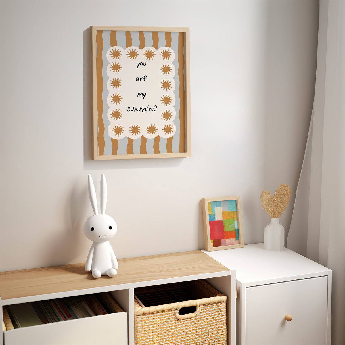My sunshine sun border nursery print in an oak frame above a kids cubby shelf with a woven basket and bunny lamp