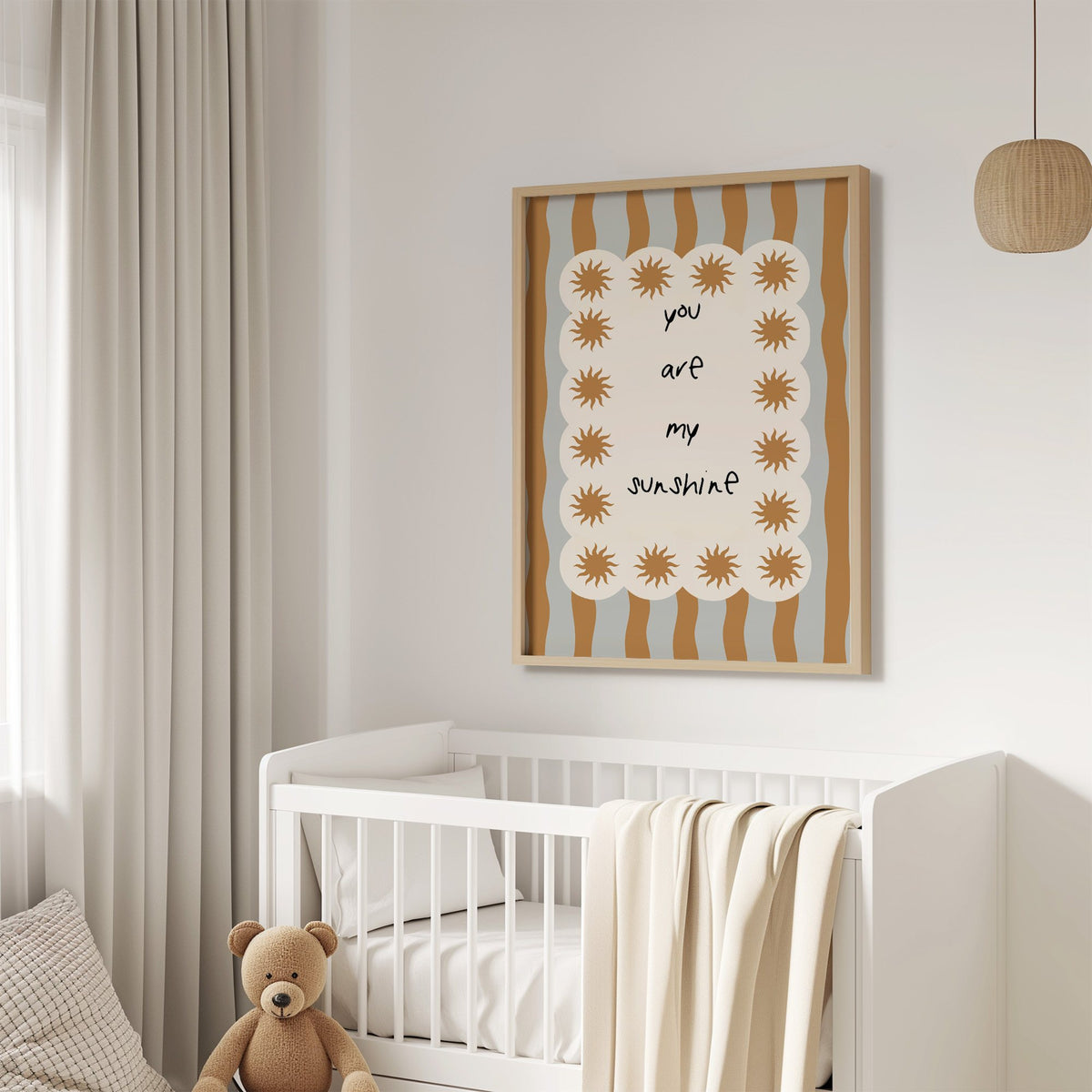 My sunshine sun border nursery print in an oak frame above a white crib with a teddy bear