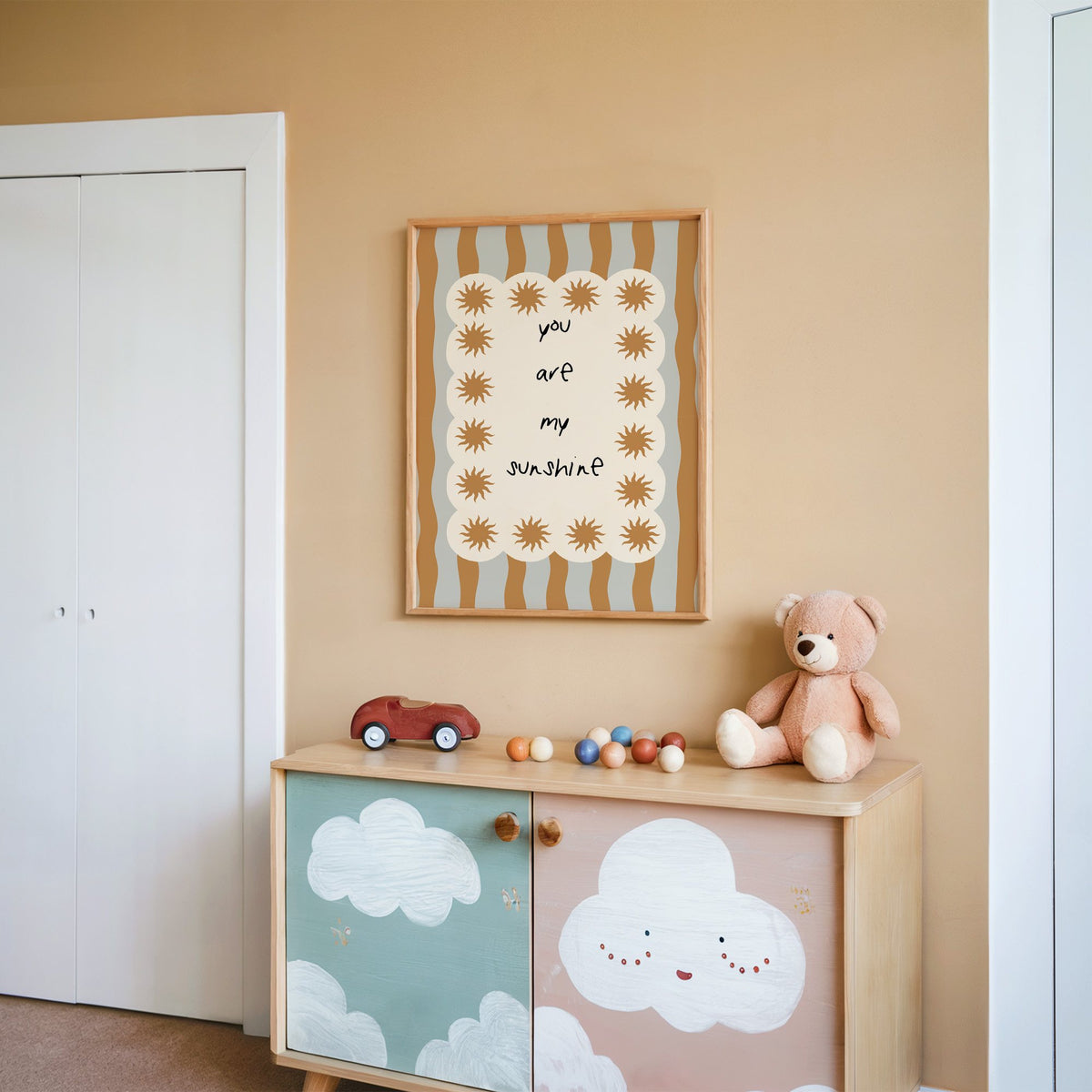 My sunshine sun border nursery print in an oak frame on a peach wall above a cloud-painted cabinet