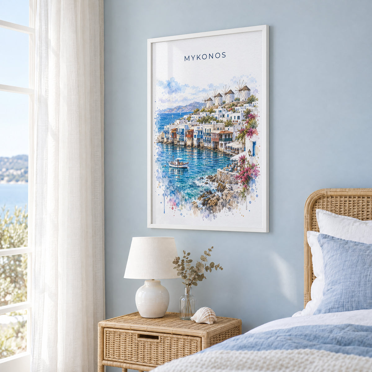 Mykonos watercolor print in a white frame on a pale blue wall beside a rattan bed in a coastal bedroom
