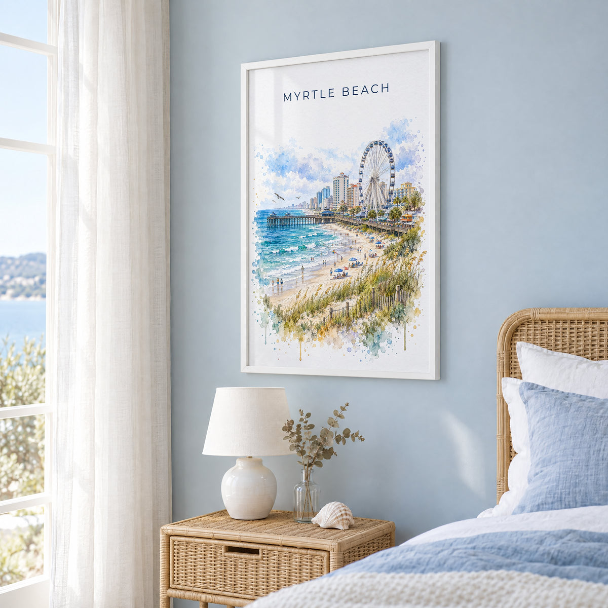 Myrtle Beach watercolor print in a white frame on a pale blue wall beside a rattan bed in a coastal bedroom