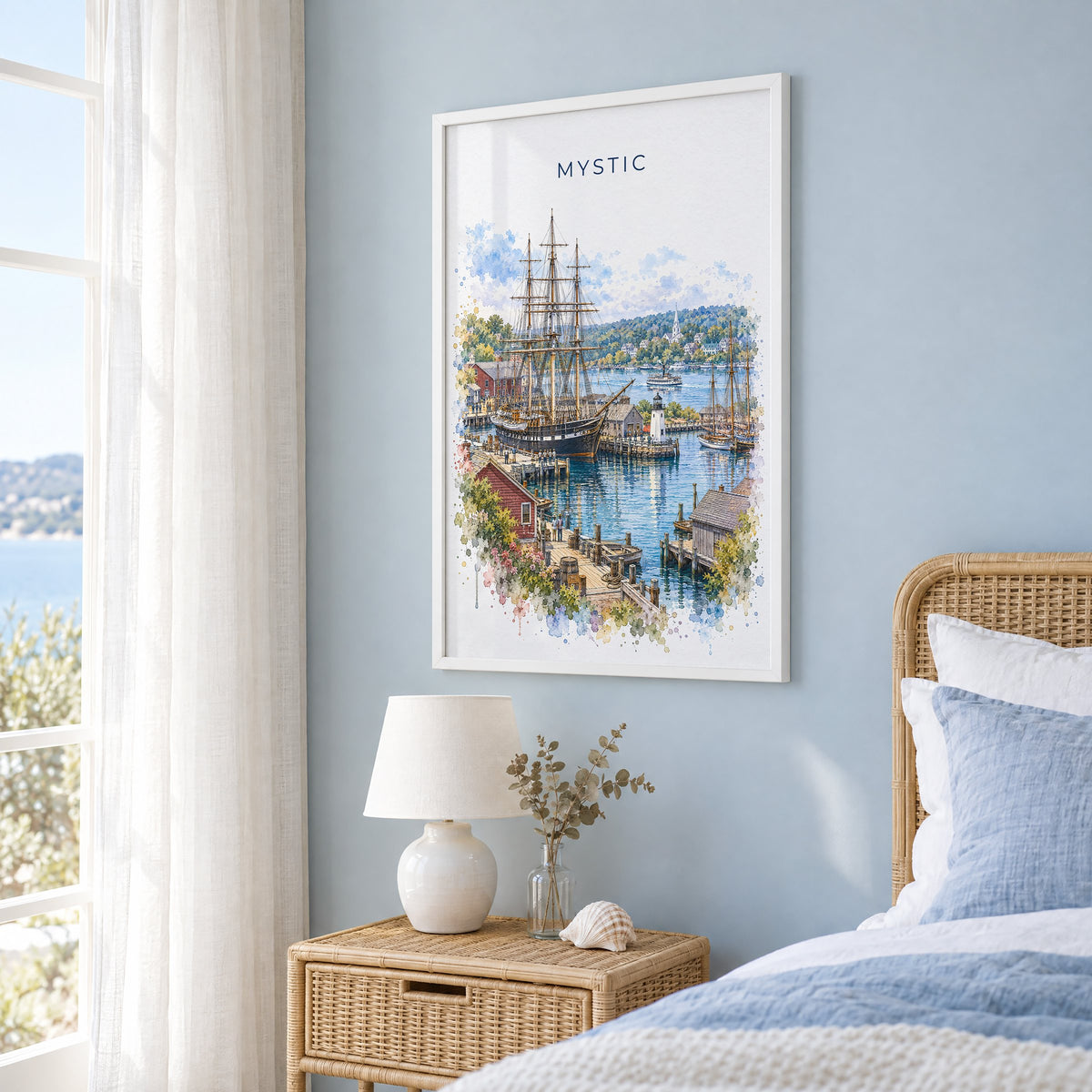 Mystic, Connecticut watercolor print in a white frame on a pale blue wall beside a rattan bed in a coastal bedroom