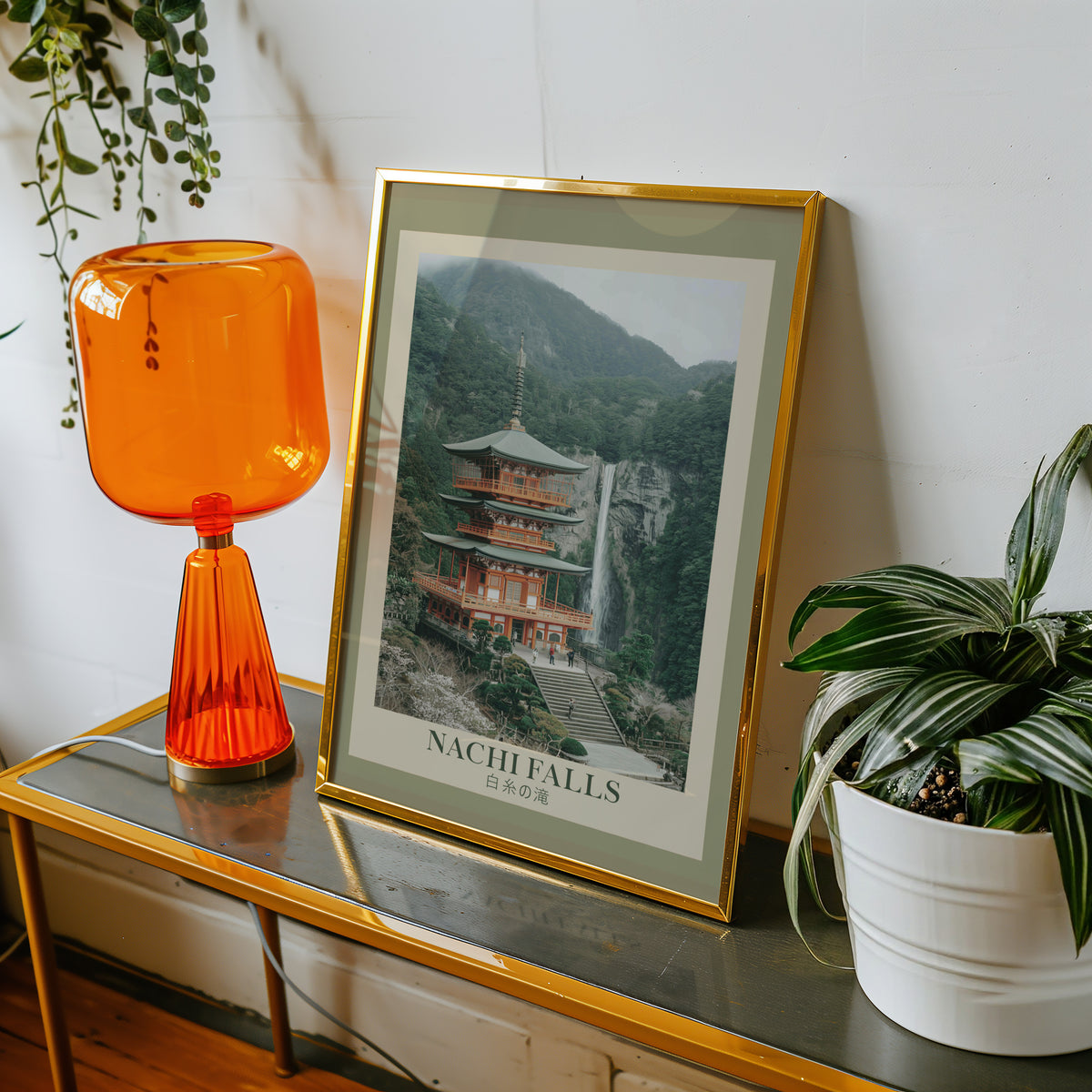 Nachi Falls and red pagoda print shown in a gold frame on a console beside an orange glass lamp