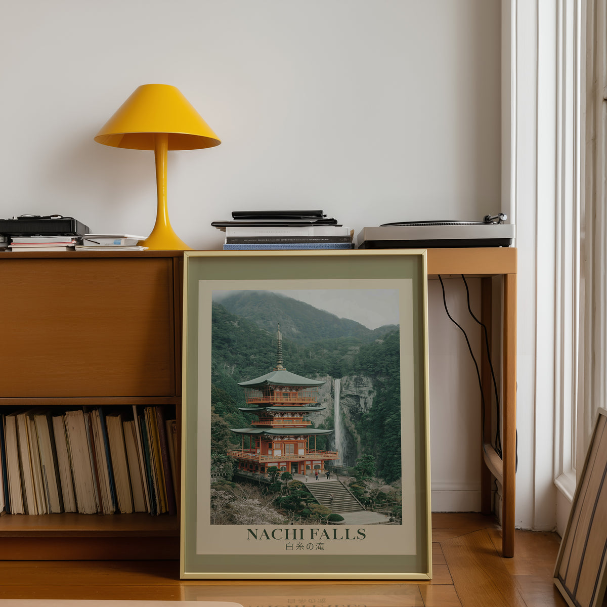 Nachi Falls and red pagoda print shown in a gold frame below a teak desk with a yellow lamp