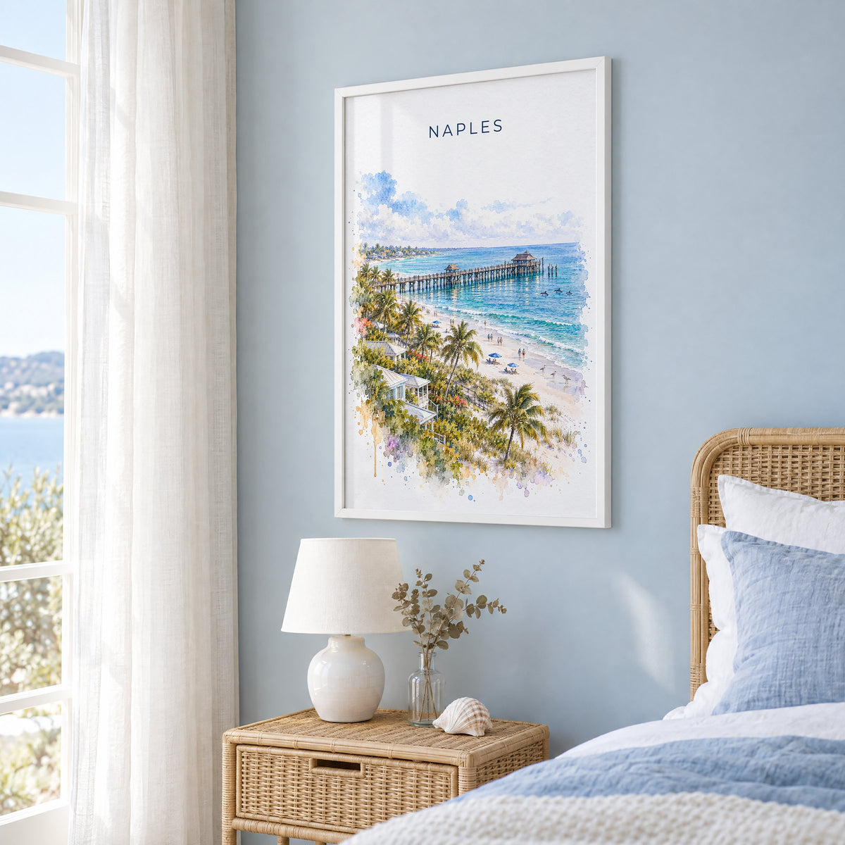 Naples, Florida watercolor print in a white frame on a pale blue wall beside a rattan bed in a coastal bedroom