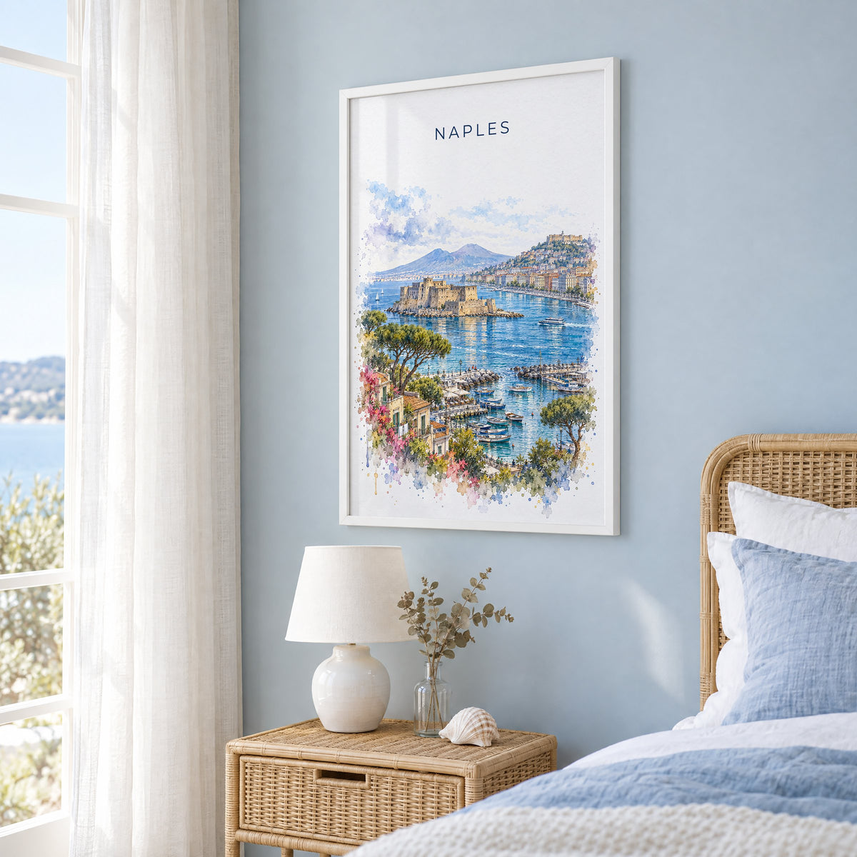 Naples, Italy watercolor print in a white frame on a pale blue wall beside a rattan bed in a coastal bedroom