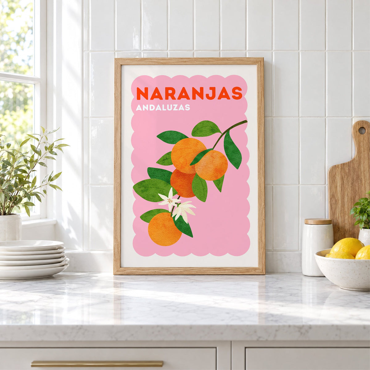 Naranjas Andaluzas orange branch print in an oak frame leaning on a marble counter by white tiles and lemons
