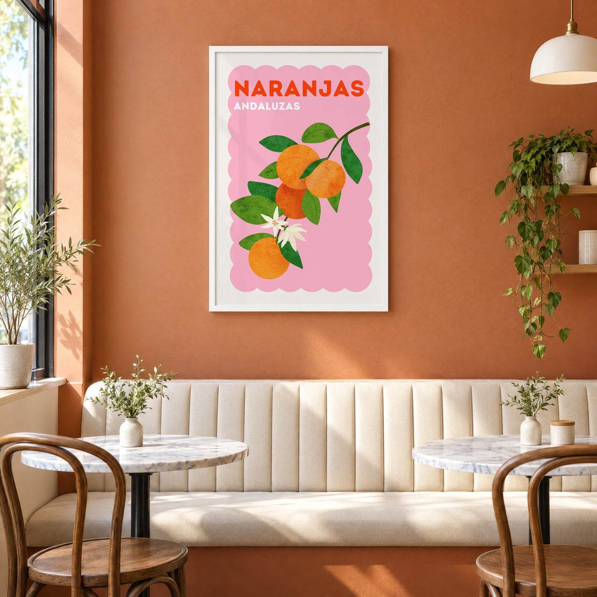 Naranjas Andaluzas orange branch print in a white frame above a cream banquette on a terracotta cafe wall