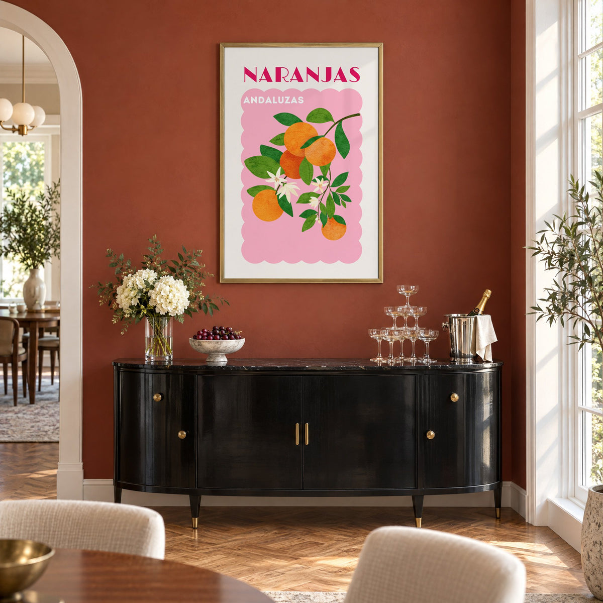 NARANJAS ANDALUZAS orange branch print in a brass frame on a terracotta wall above a black buffet with a champagne tower