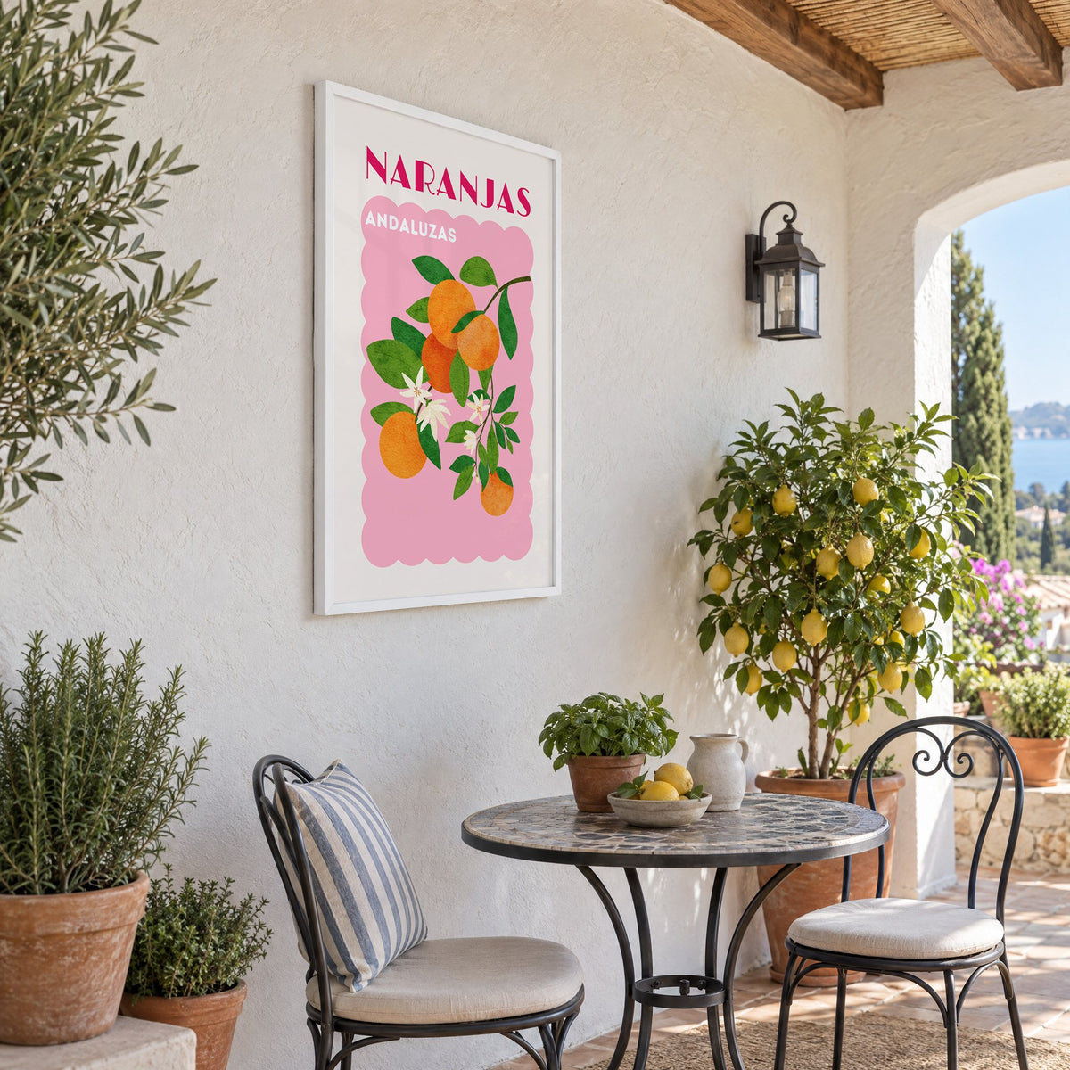 NARANJAS ANDALUZAS orange branch print in a white frame on a sunny patio wall beside a potted lemon tree