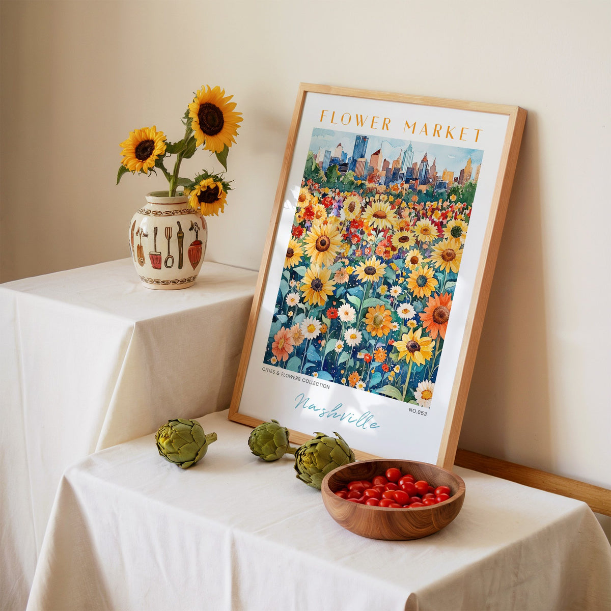 Nashville flower market print in an oak frame leaning on a linen-draped table beside a vase of sunflowers