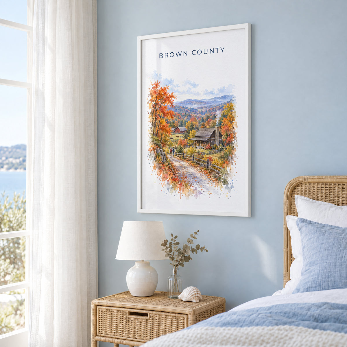 Nashville, Indiana watercolor print in a white frame on a pale blue wall beside a rattan bed in a coastal bedroom