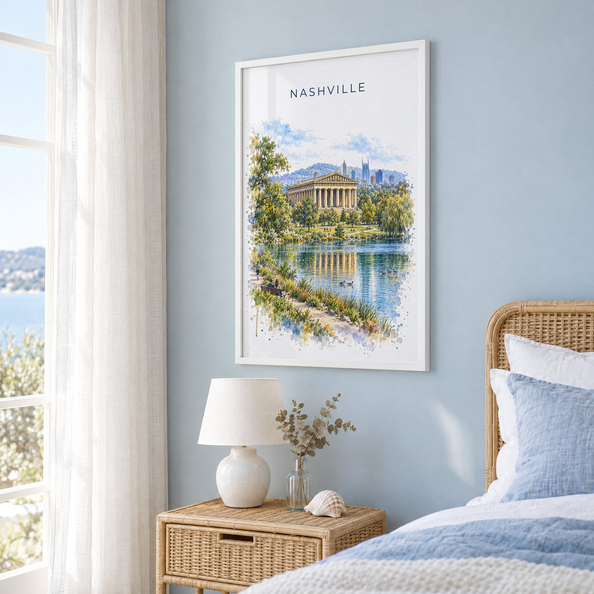 Nashville Parthenon watercolor print in a white frame on a pale blue wall beside a rattan bed in a coastal bedroom