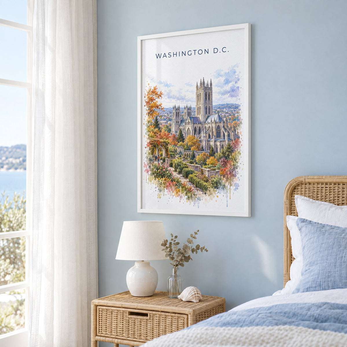 Washington National Cathedral watercolor print in a white frame on a pale blue wall beside a rattan bed in a coastal bedroom