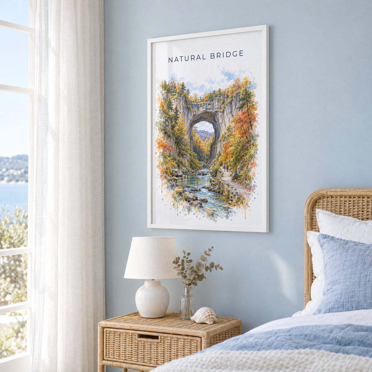 Natural Bridge, Virginia watercolor print in a white frame on a pale blue wall beside a rattan bed in a coastal bedroom