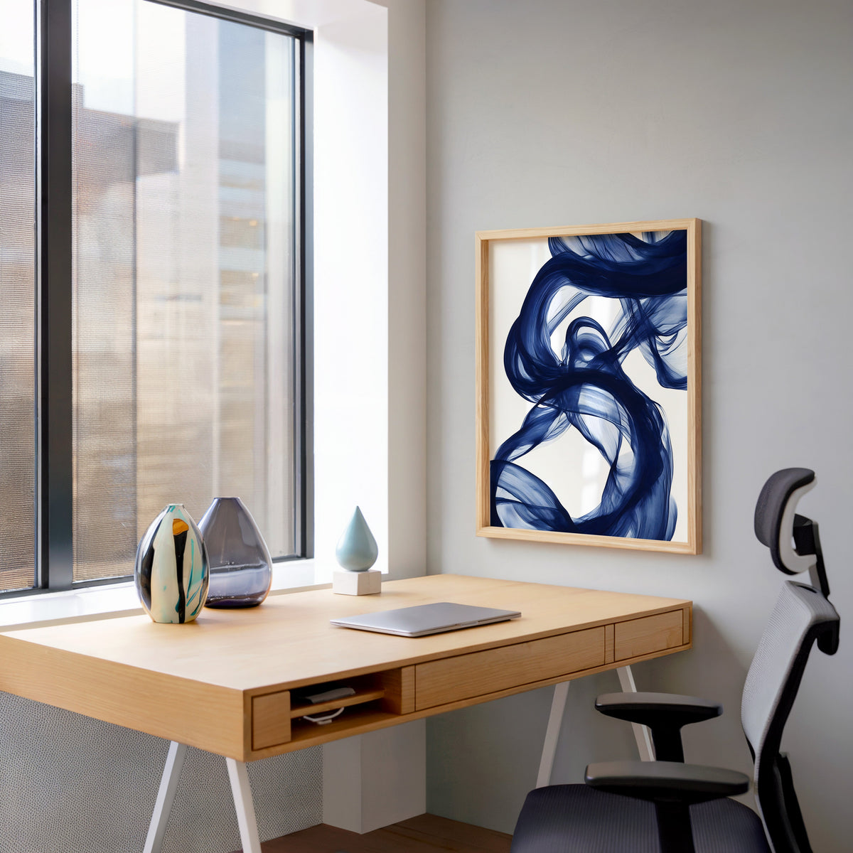 Navy blue silk swirl fluid abstract print in a pale wood frame above a home office desk by a tall window