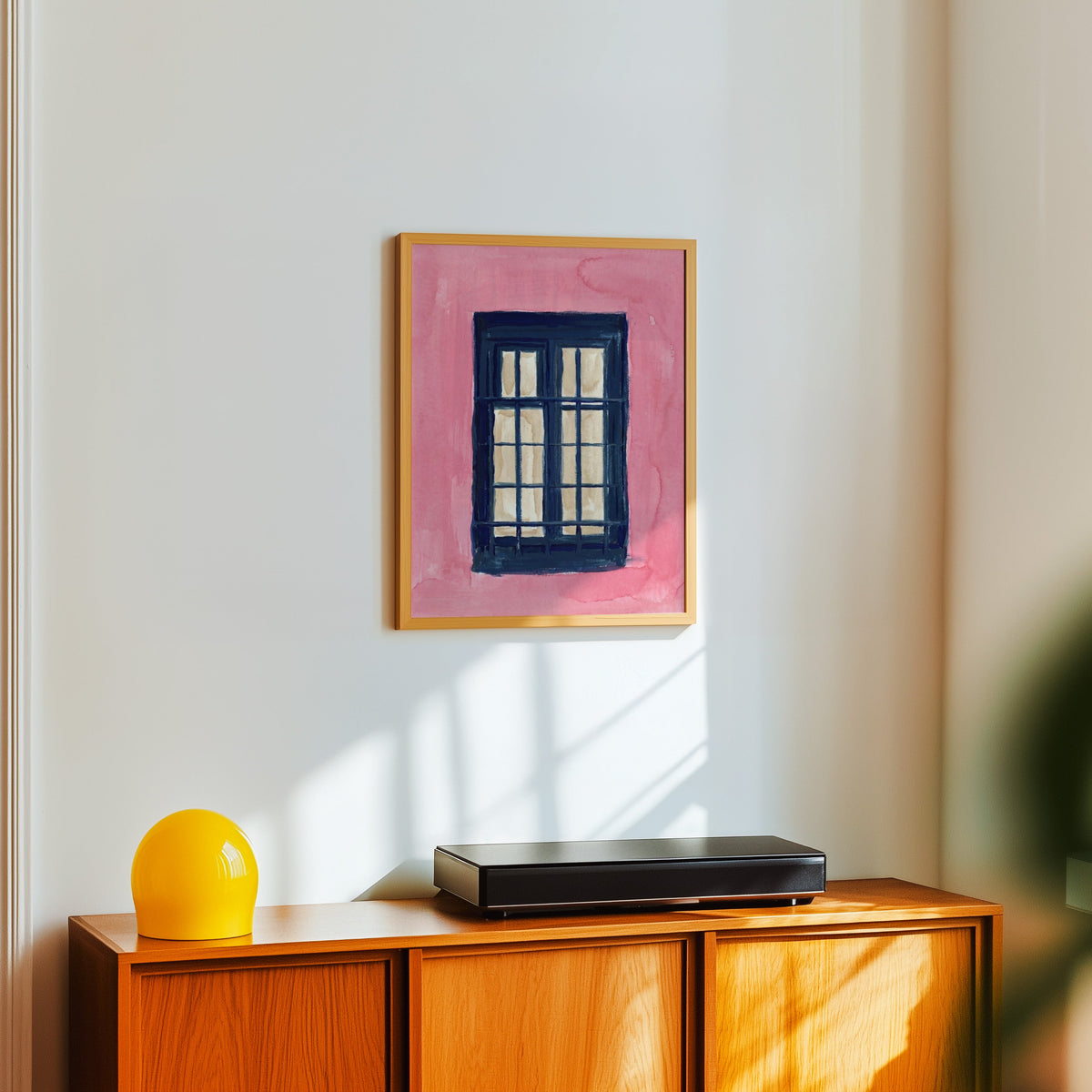 Mediterranean window print in a light oak frame above a teak sideboard with a yellow lamp