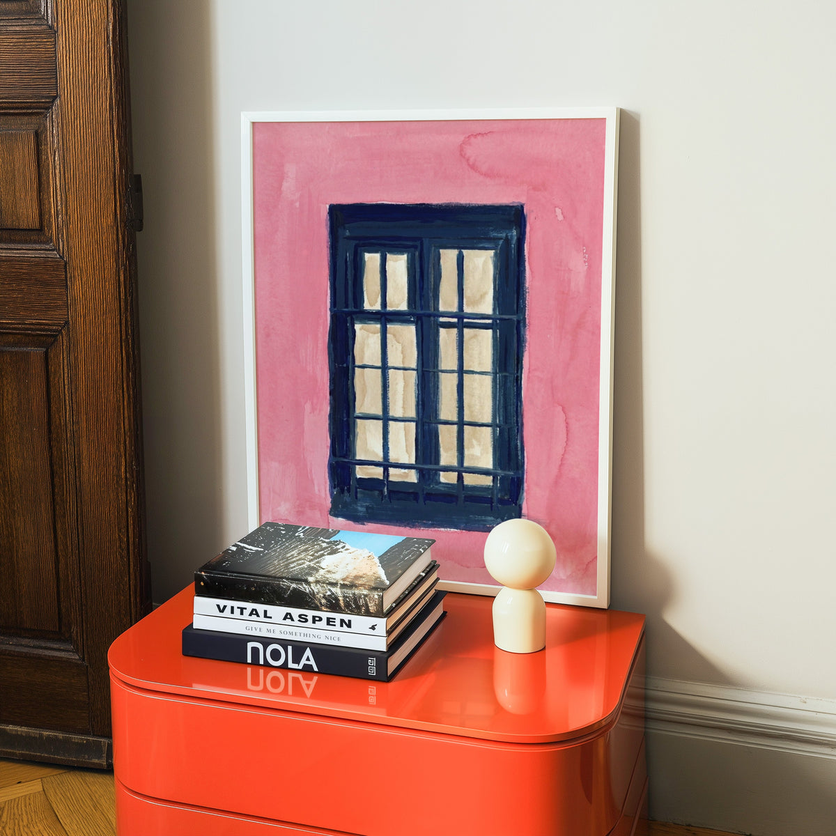 Architectural window print in a white frame on a glossy orange cabinet with books