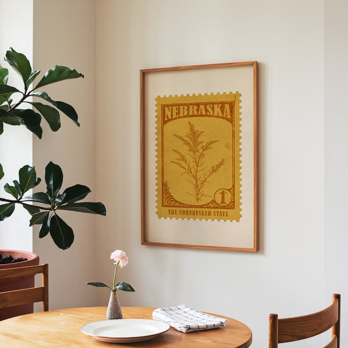 Nebraska state flower print framed above a round wooden table with a single bloom in a vase and books