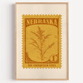Nebraska state flower stamp print in ochre brown on mustard, light oak frame on a plain white wall