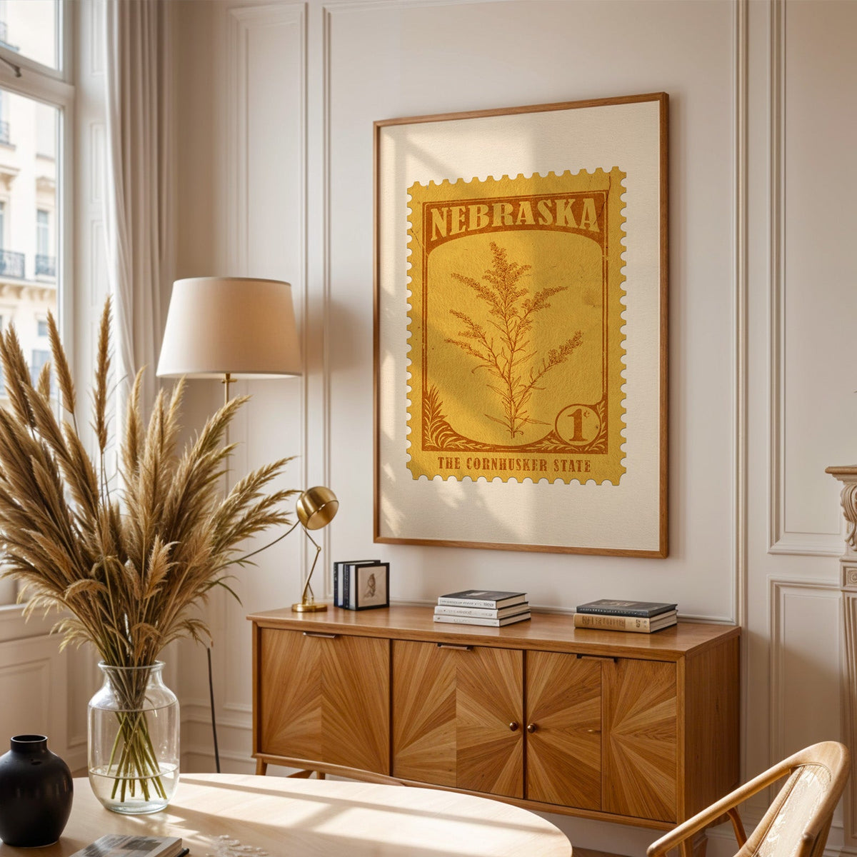 Nebraska stamp print framed above a wooden sideboard, pampas grass in a glass vase and a floor lamp