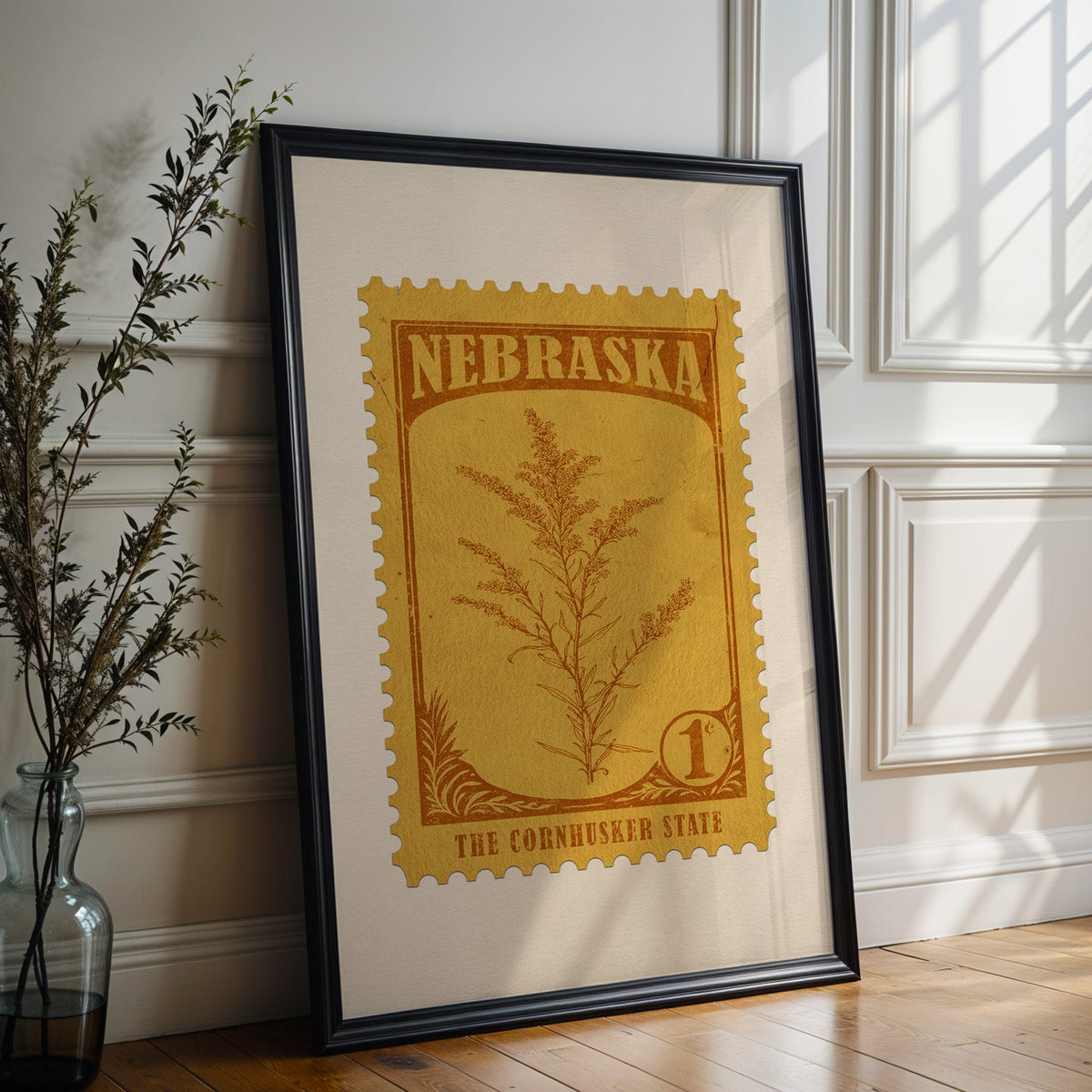 Nebraska state flower print in a black frame leaning against a white panelled wall beside olive branches