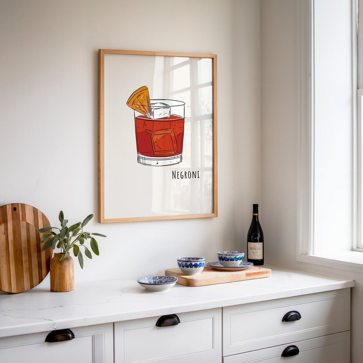 Negroni line print in an oak frame above a white sideboard with a bottle of wine