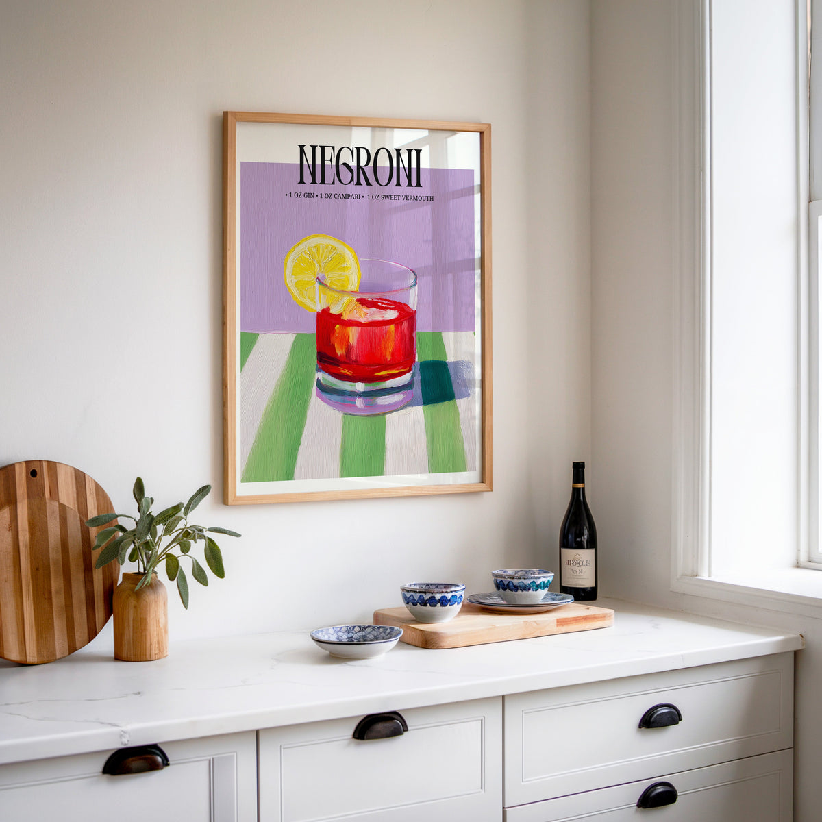 Negroni painterly print in an oak frame above a white sideboard with a bottle of wine