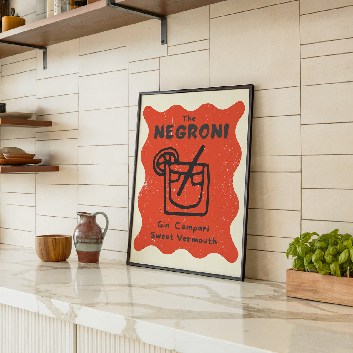 Negroni print in a black frame leaning on a marble counter in a tiled kitchen