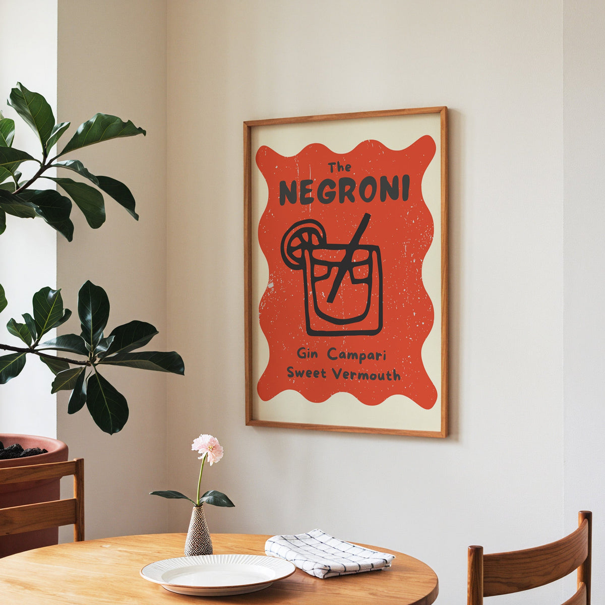 Negroni print in a walnut frame above a round table beside a fiddle-leaf fig