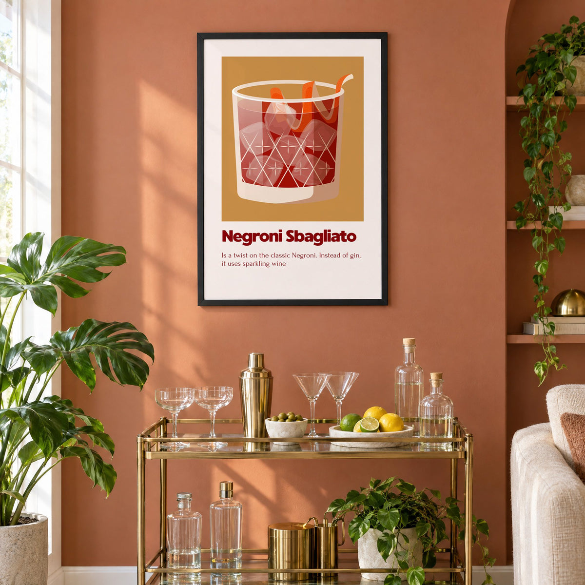 Negroni Sbagliato rocks glass ochre card print in a black frame on a terracotta wall above a brass bar cart with coupes and citrus