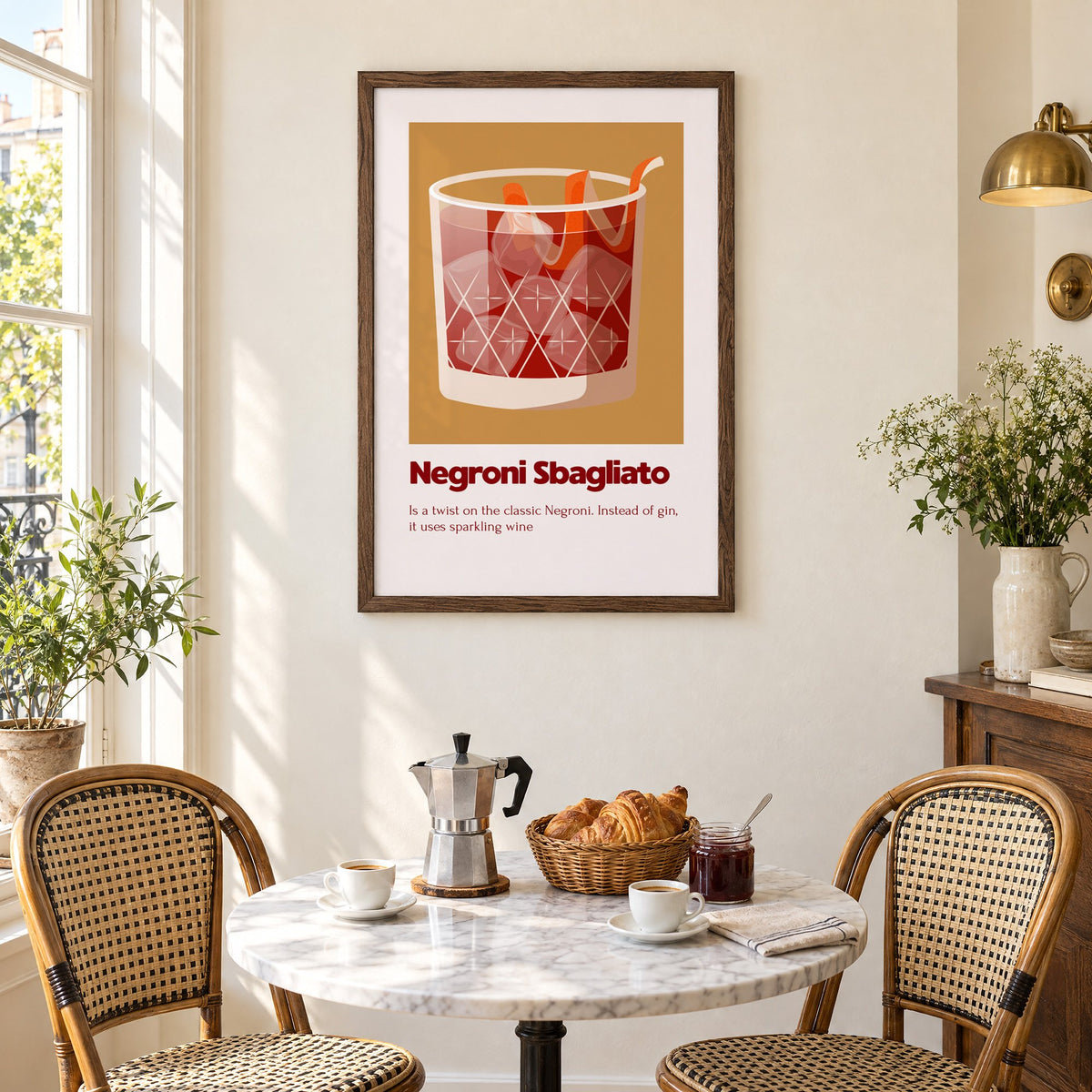 Negroni Sbagliato rocks glass ochre card print in a walnut frame above a marble bistro table with croissants and rattan chairs