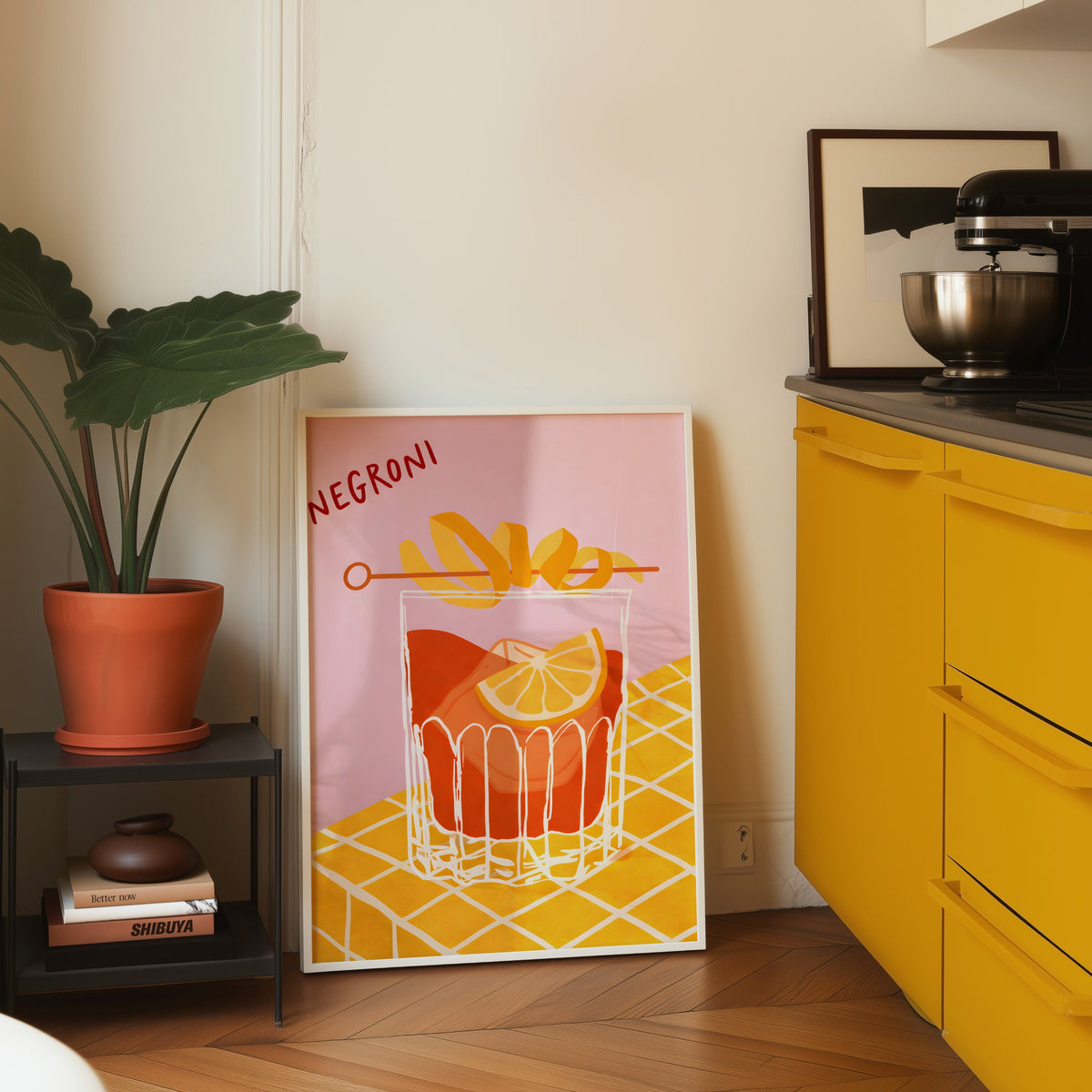 Negroni print in a white frame leaning on parquet beside a bright yellow kitchen