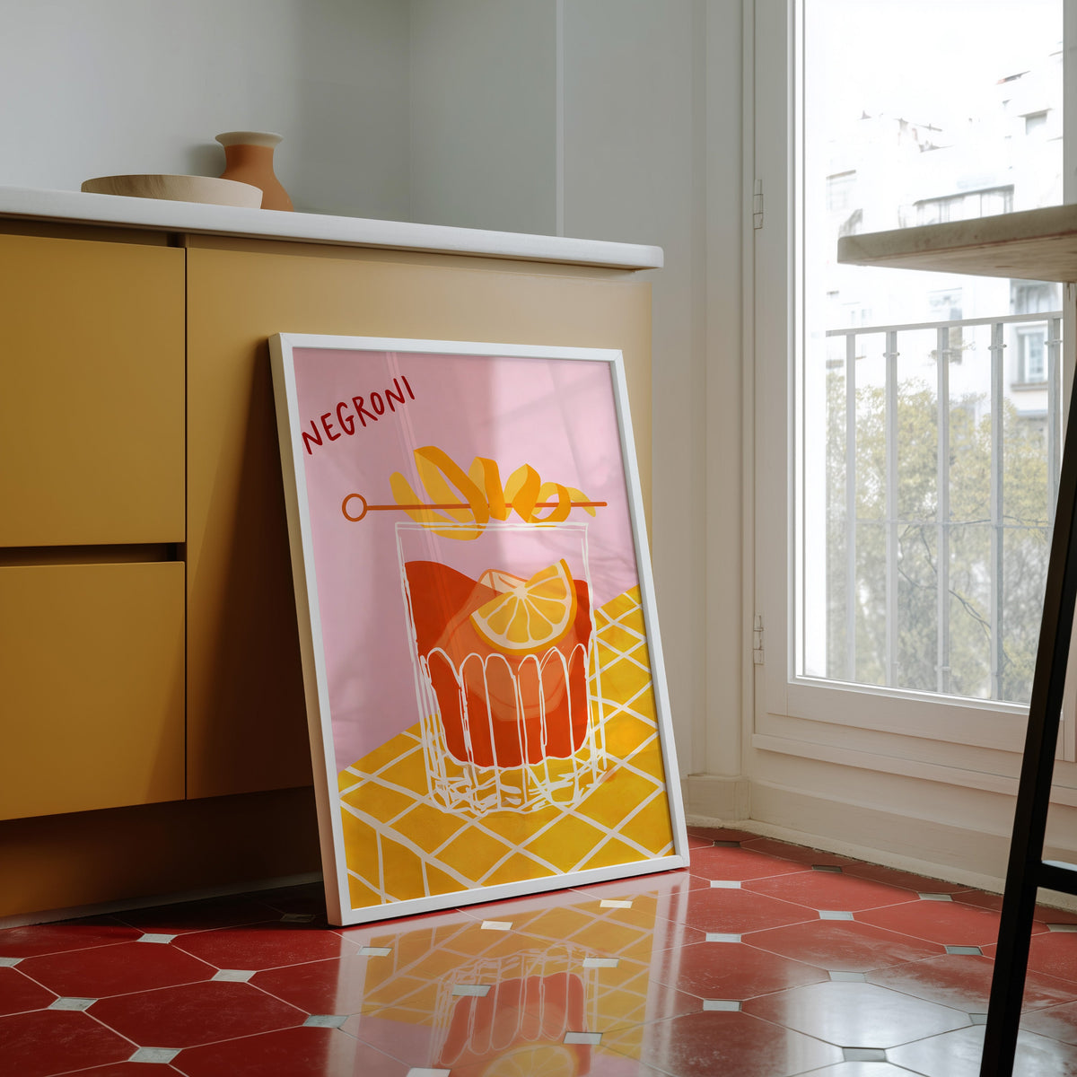 Negroni print in a white frame against yellow cabinets on a red tiled floor