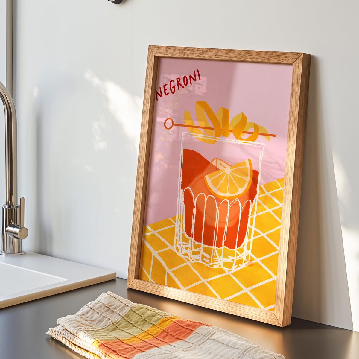 Negroni print in an oak frame by the kitchen sink beside a striped tea towel