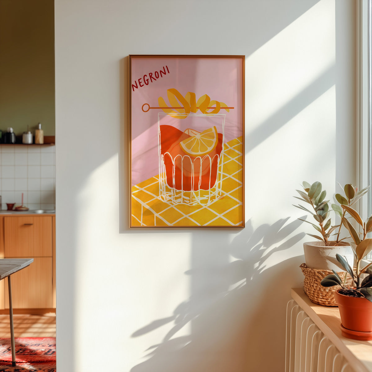 Negroni print in a gold frame in sunlight with plants and a kitchen beyond