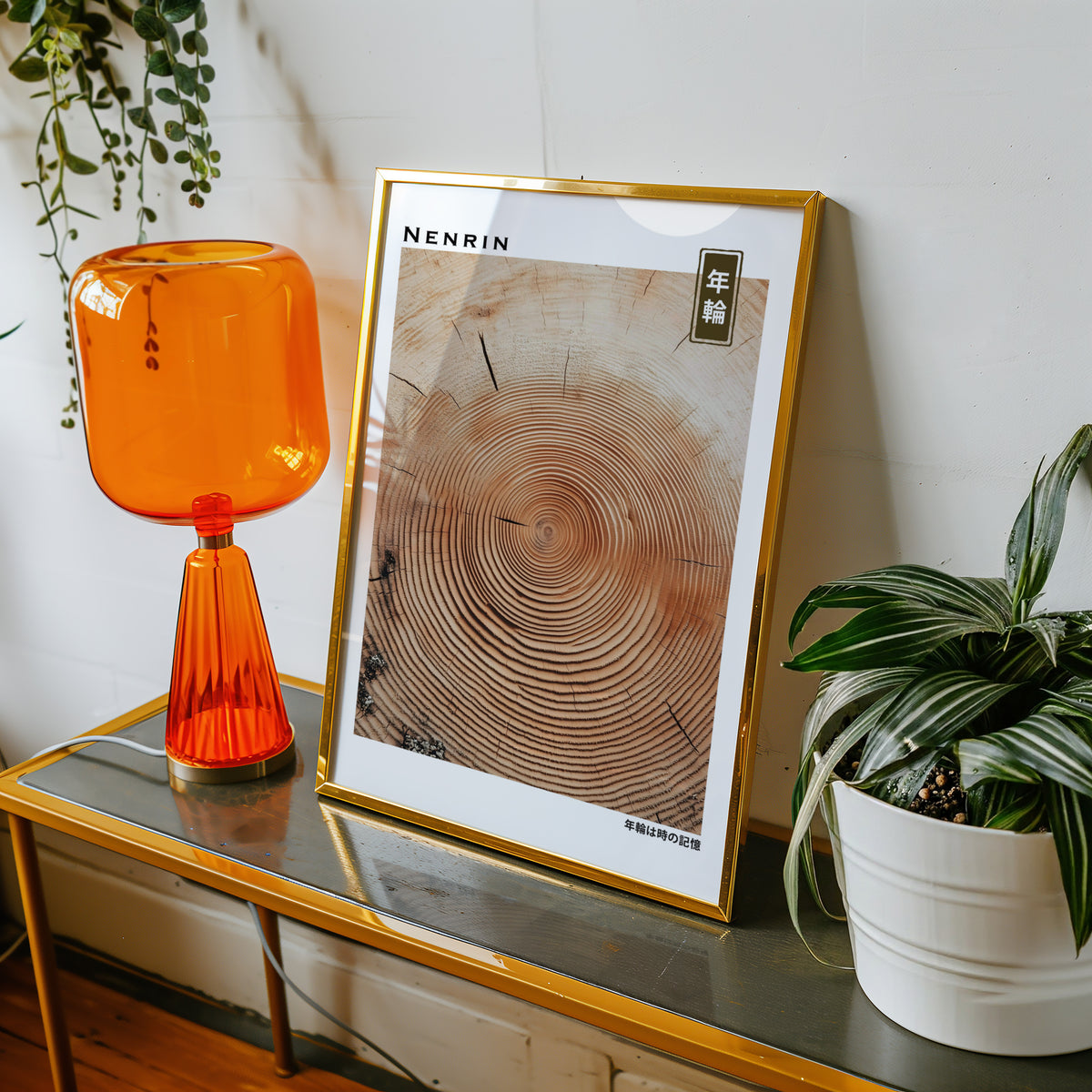 Orange-brown wood slice tree rings print shown in a gold frame on a console beside an orange glass lamp