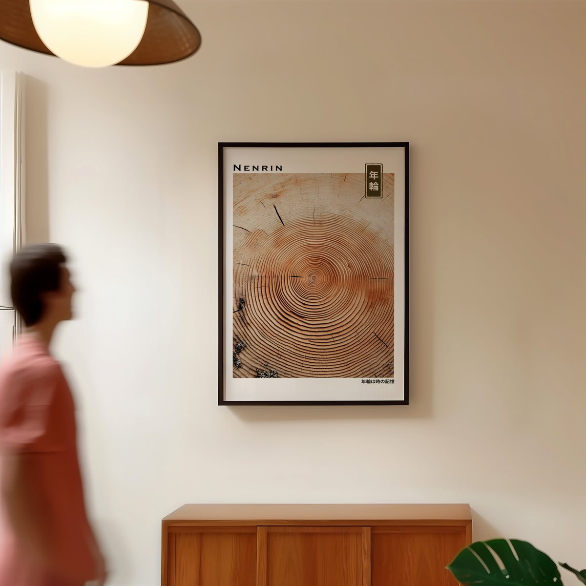 Orange-brown wood slice tree rings print in a black frame in a hallway under a rattan pendant