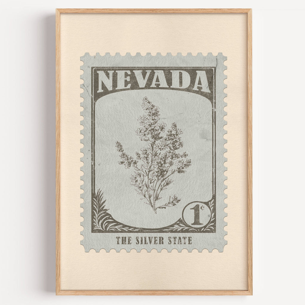 Nevada state flower stamp print in warm grey on pale grey-green, light oak frame on a plain white wall