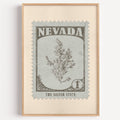 Nevada state flower stamp print in warm grey on pale grey-green, light oak frame on a plain white wall
