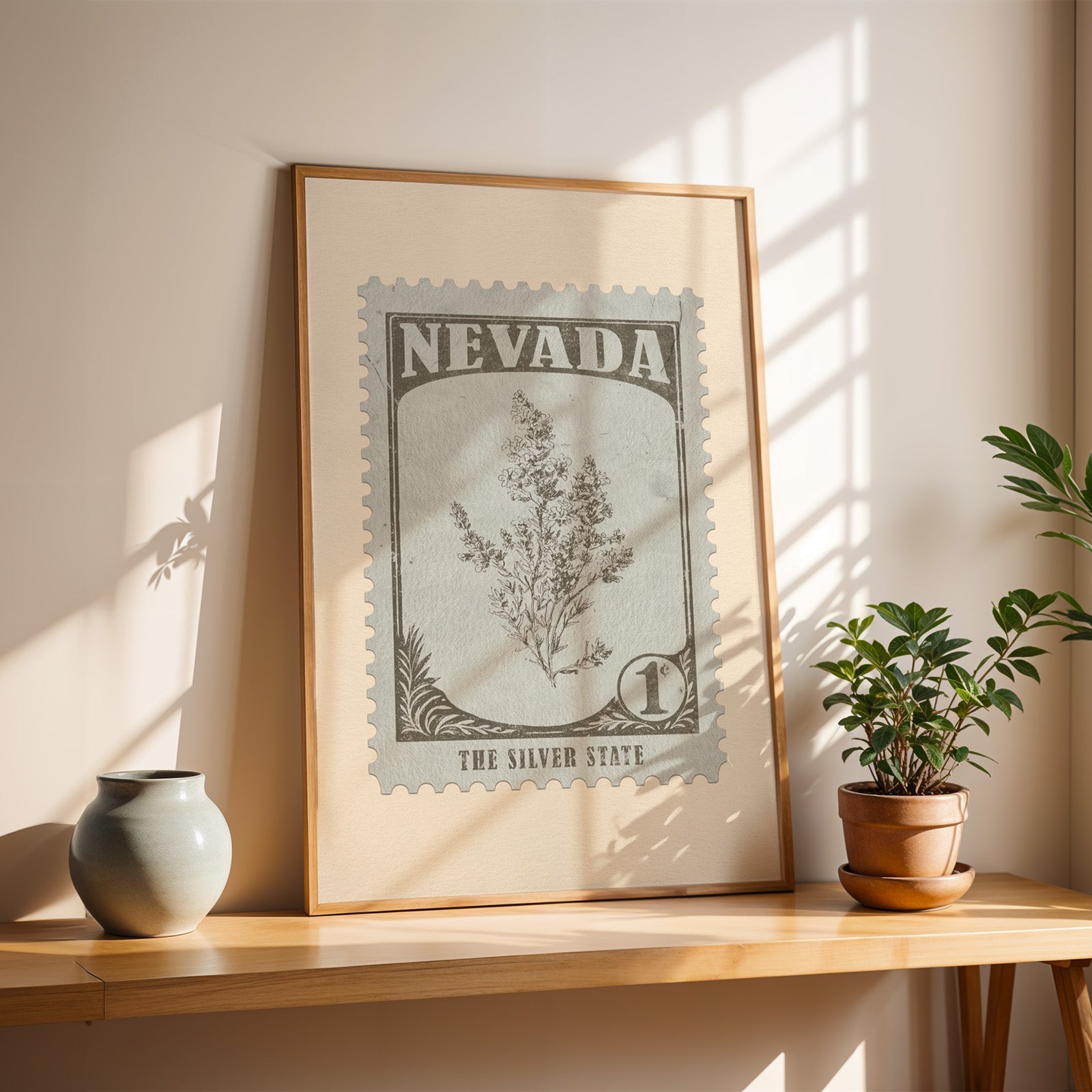 Nevada sagebrush stamp print in a light oak frame leaning on a wooden table beside a stoneware vase